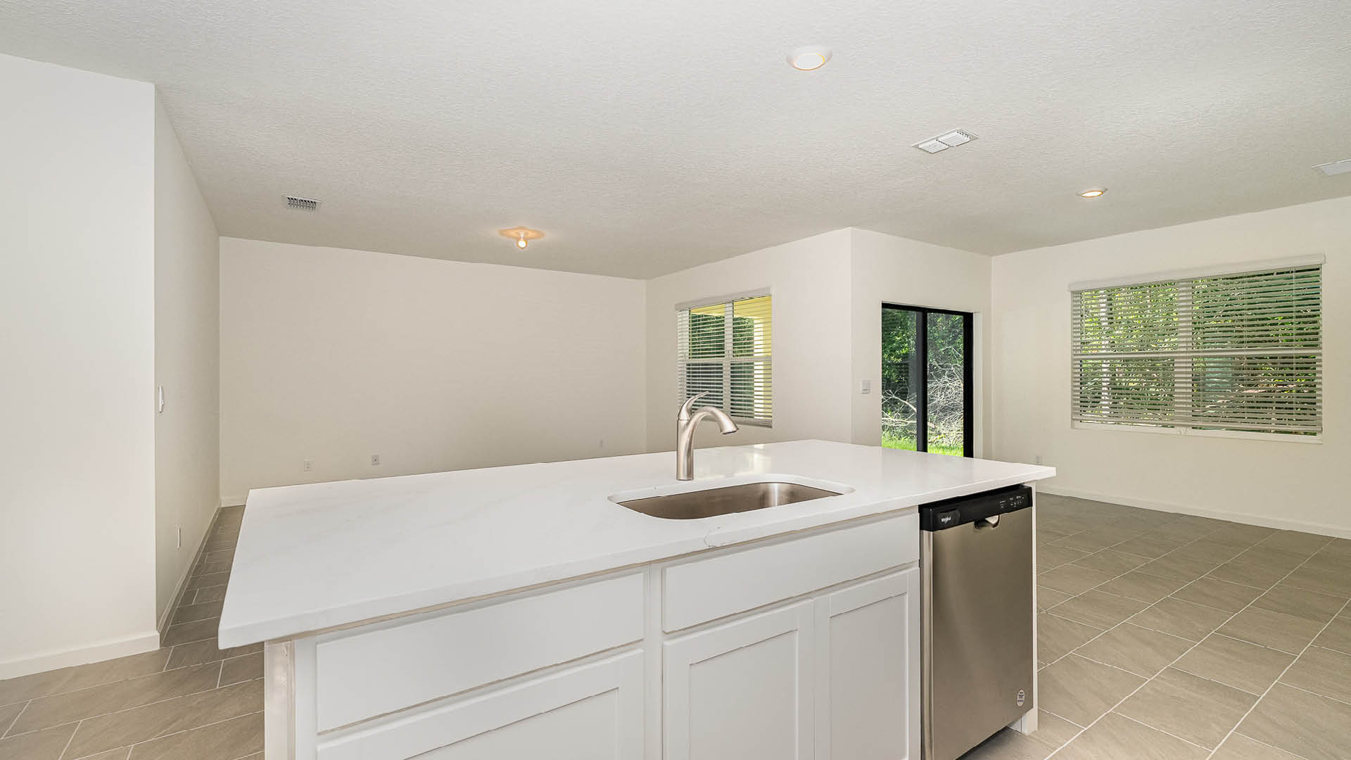 Modern kitchen with an island, white cabinetry, and stainless steel appliances, leading to a spacious living area with large windows.