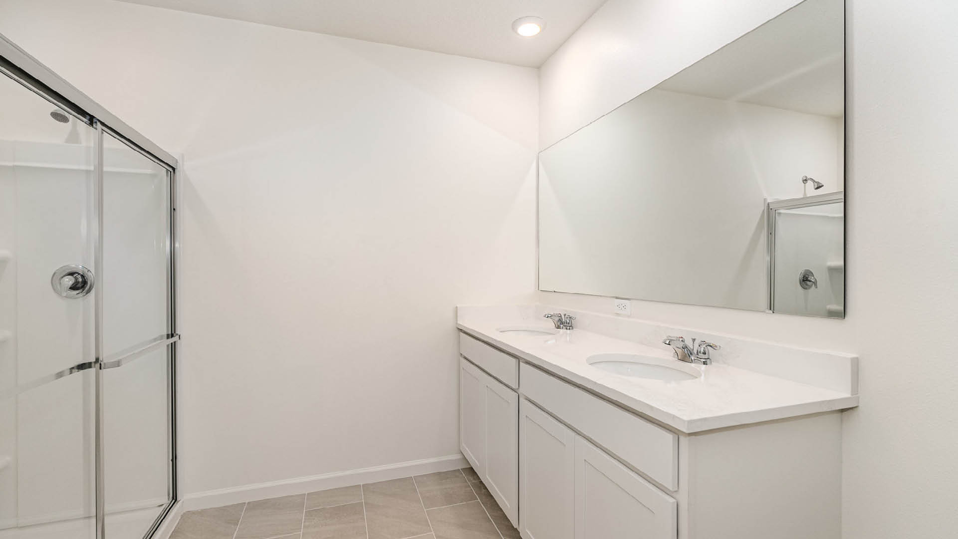 Bright modern bathroom featuring a double sink vanity, large mirror, and a glass shower. Neutral colors and tile flooring enhance the space.
