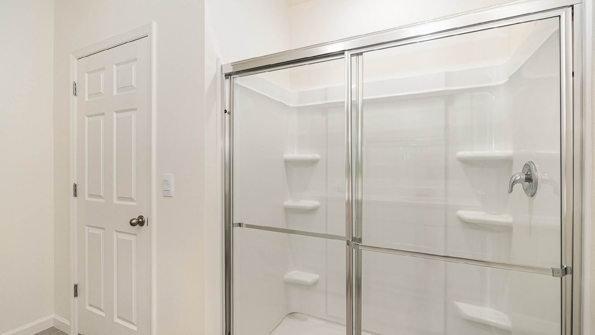 Bright, modern shower enclosed in glass with chrome fixtures, adjacent to a closed white door in a clean bathroom setting.