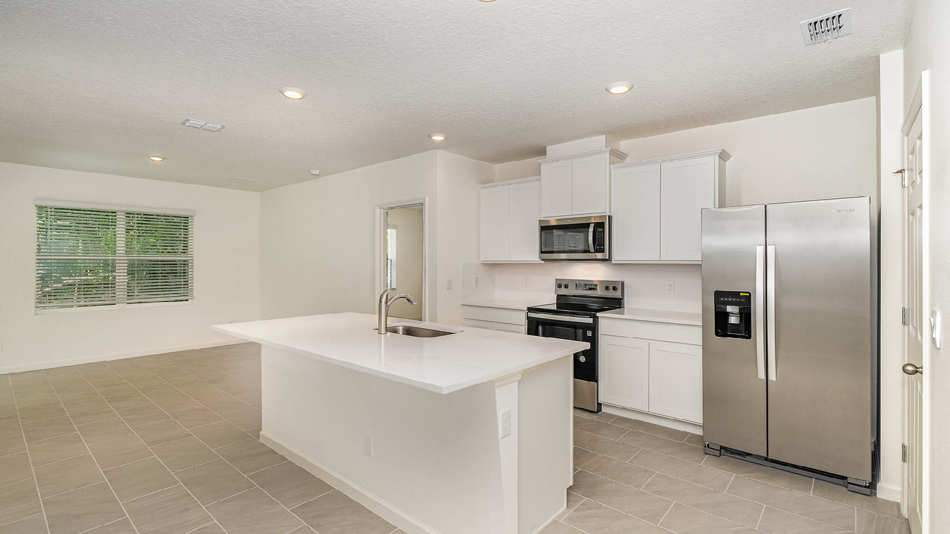 Modern kitchen with white cabinets, stainless steel appliances, and a central island; bright space with natural light from large windows.