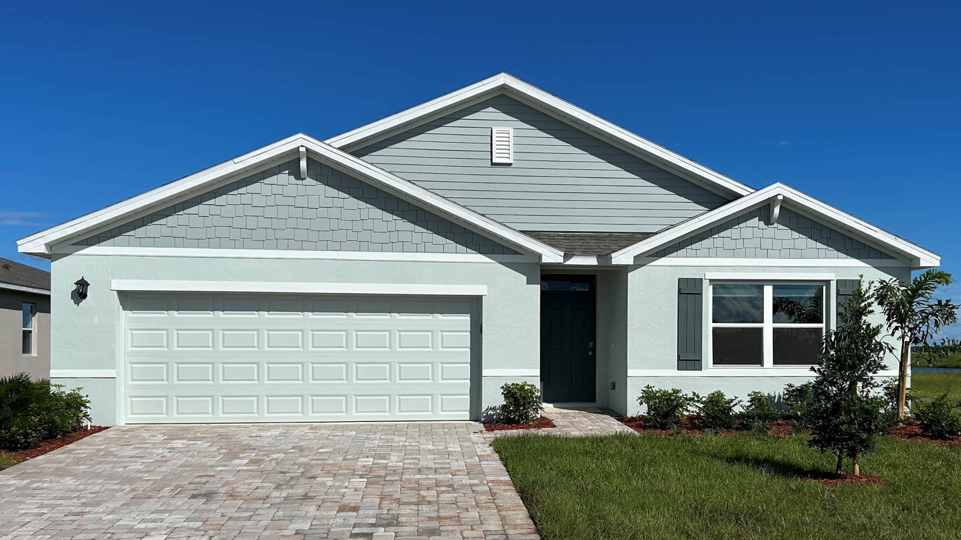 Front view of a modern, light blue house with a gray shingle accent, and a two-car garage.