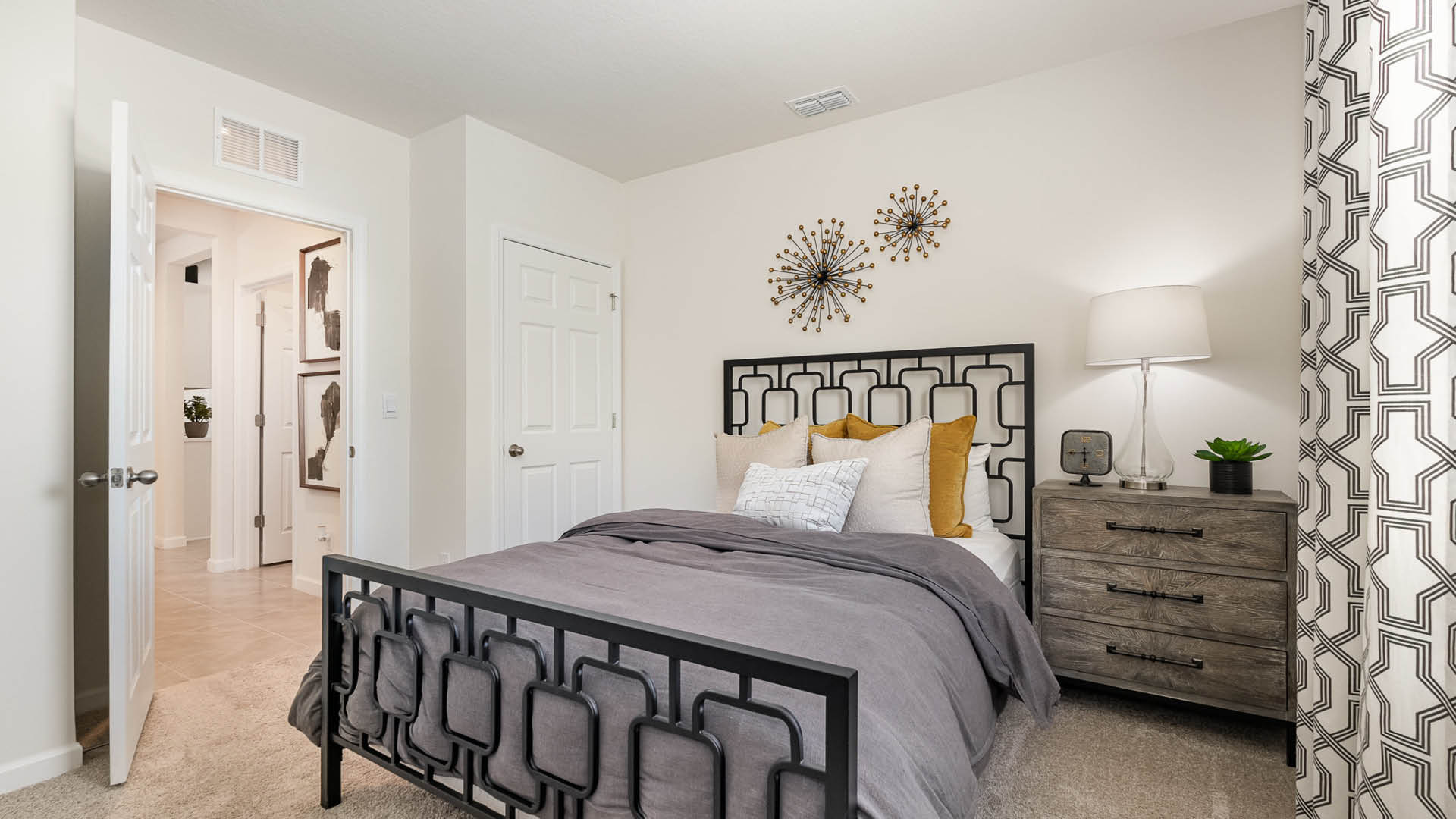 Cozy bedroom featuring a black metal bed frame, layered pillows, a modern nightstand with a lamp, and decorative wall art.