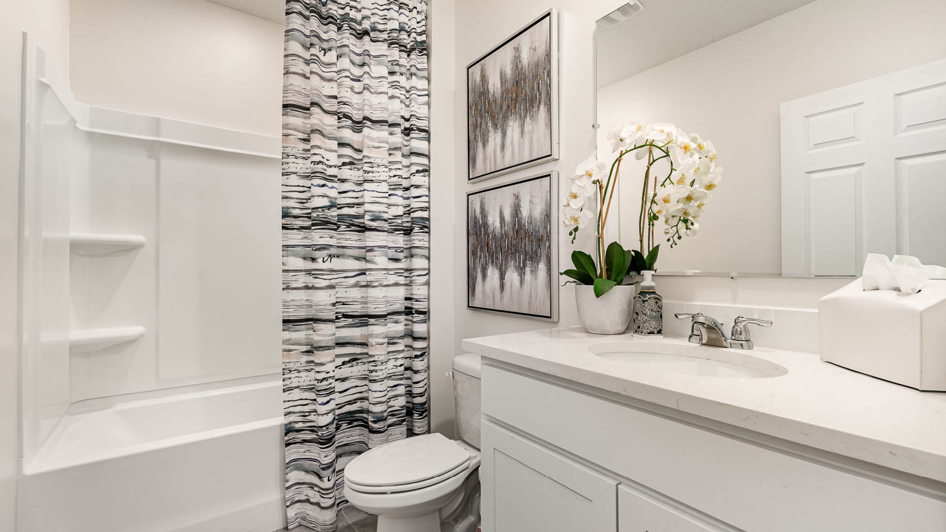 Modern bathroom featuring a shower, white vanity, decorative art, and a potted orchid on the counter for a stylish touch.