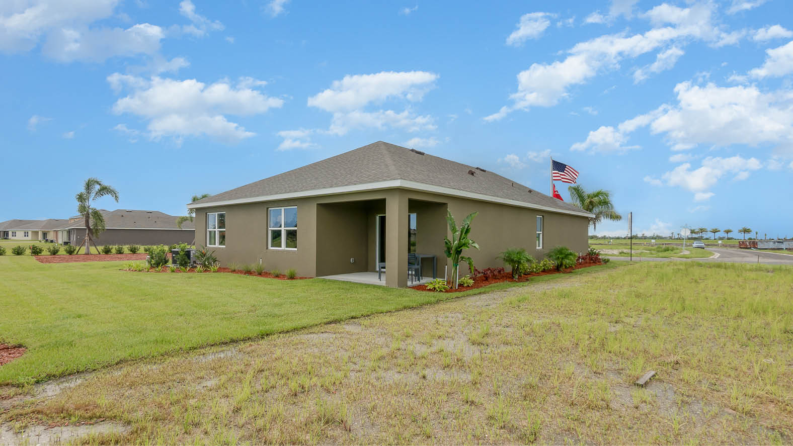A well-maintained house with a landscaped yard, featuring green grass, palm trees, and colorful plants under a bright blue sky.