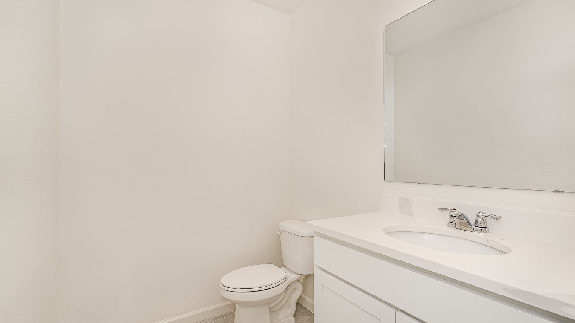 Minimalist bathroom featuring a white wall, toilet, and a sleek vanity with a mirror and faucet. Bright and uncluttered space.