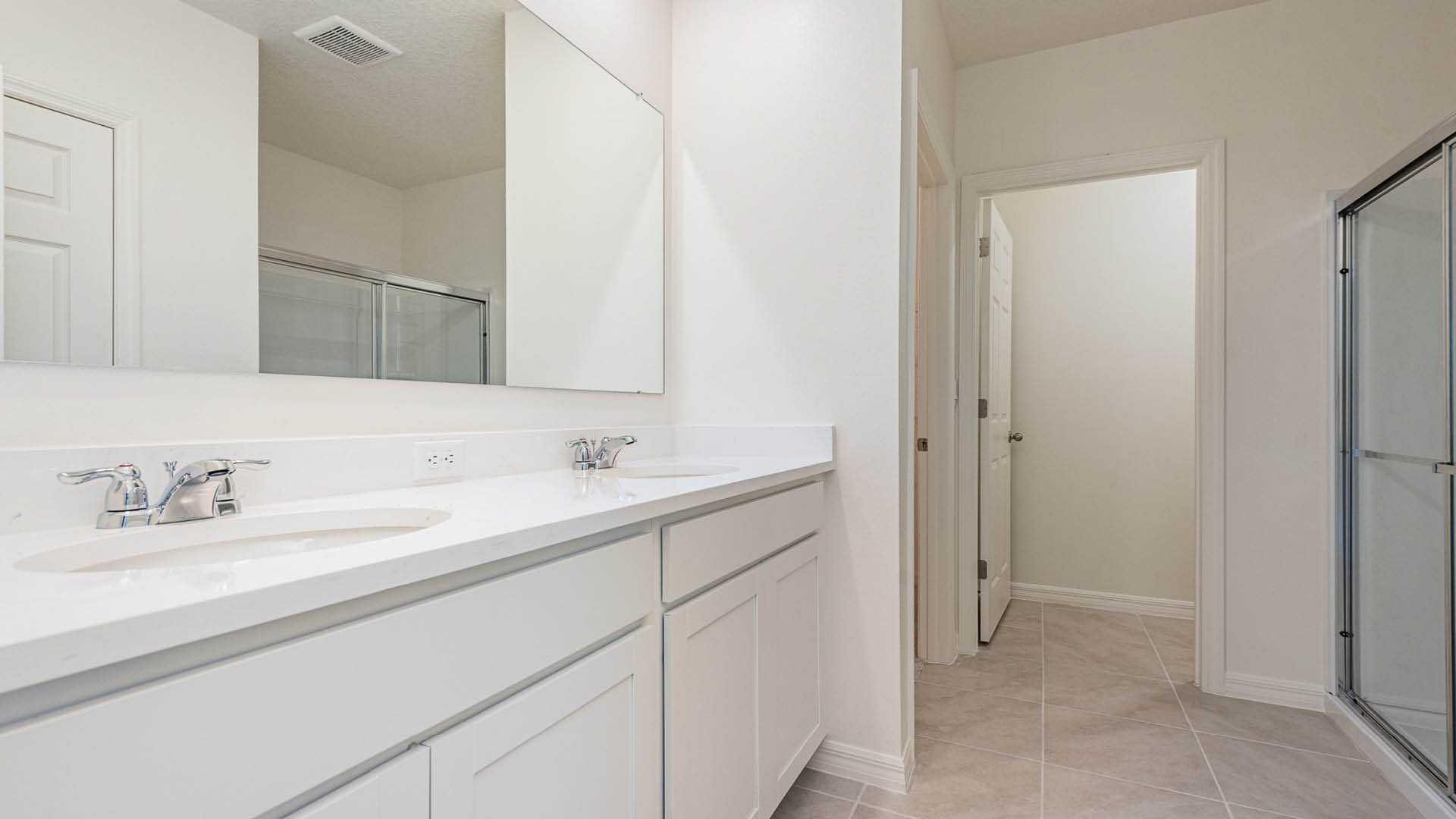 Bright, modern bathroom featuring dual sinks, a large mirror, and a glass shower enclosure against light-colored walls.