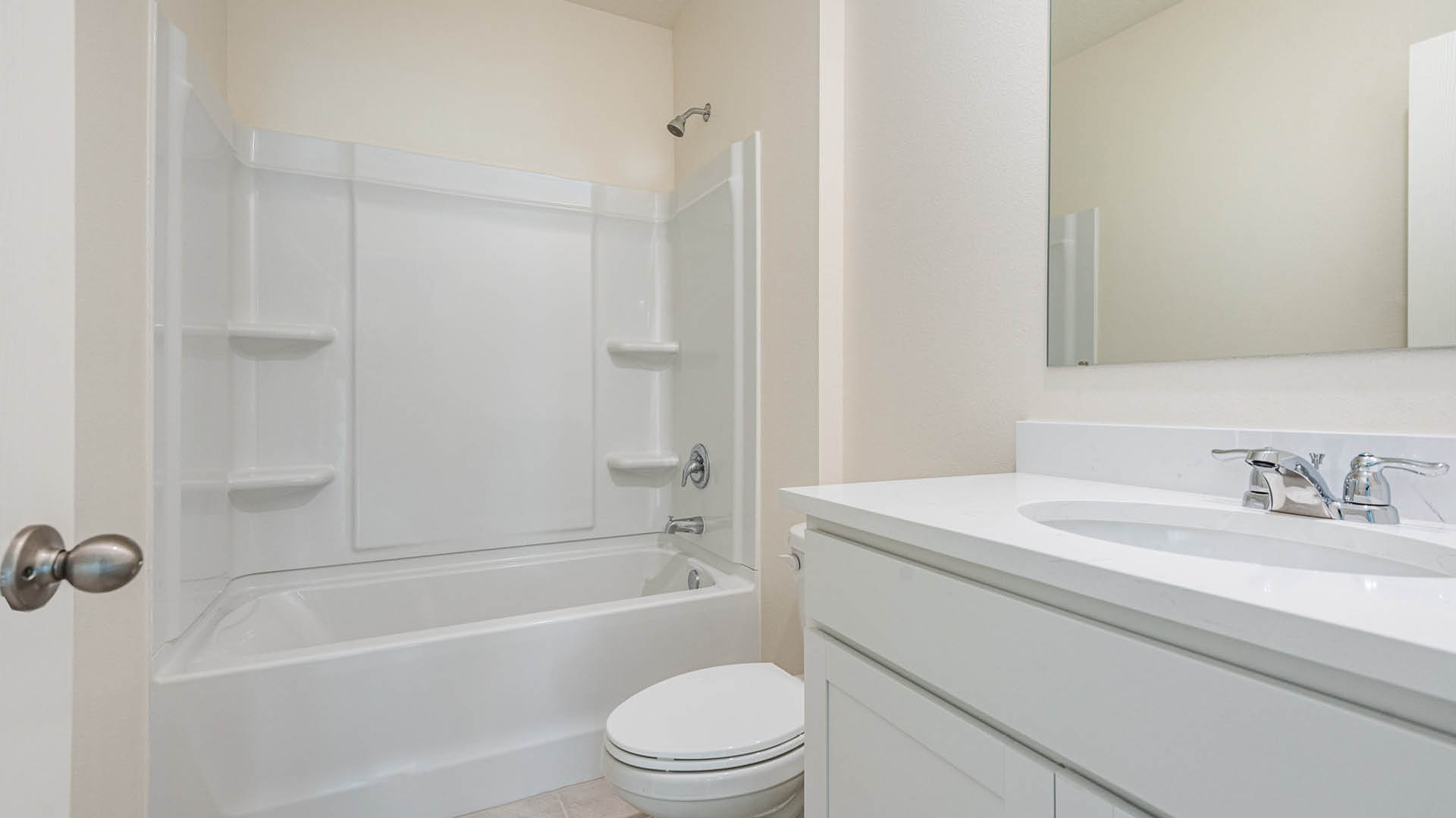 A clean, modern bathroom featuring a white bathtub-shower combo, a toilet, and a simple white vanity with a mirror above it.