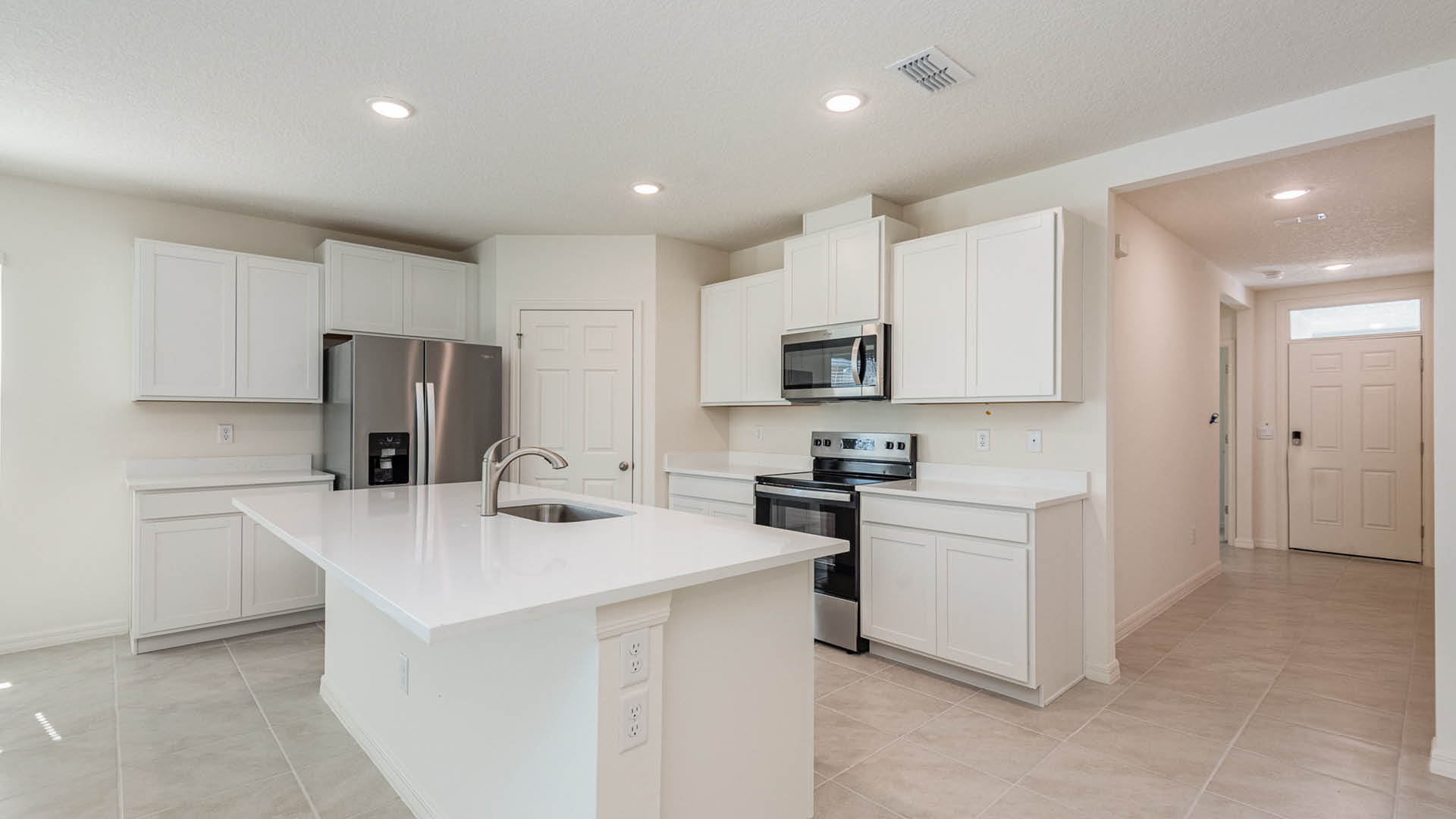Modern kitchen featuring white cabinetry, stainless steel appliances, a large island with seating, and a tiled floor. Bright and spacious design.