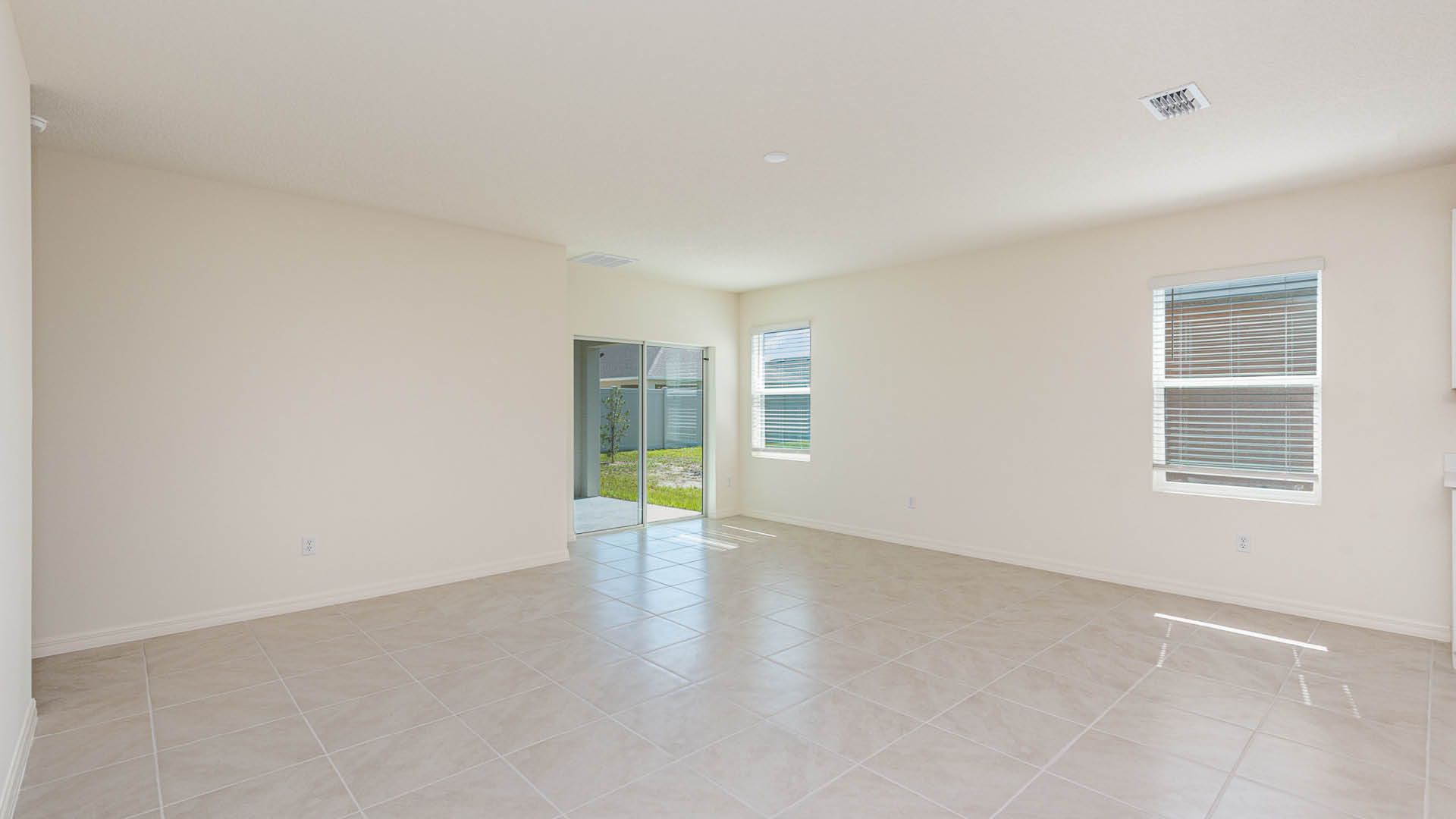 Bright, empty living room with tiled floor, large windows, and sliding glass door.