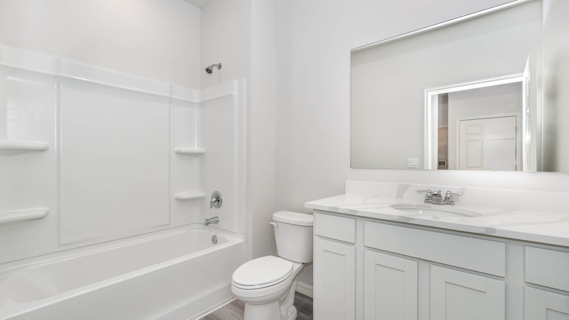 Bright and modern bathroom featuring a white tub, toilet, and double vanity with a large mirror against neutral walls.