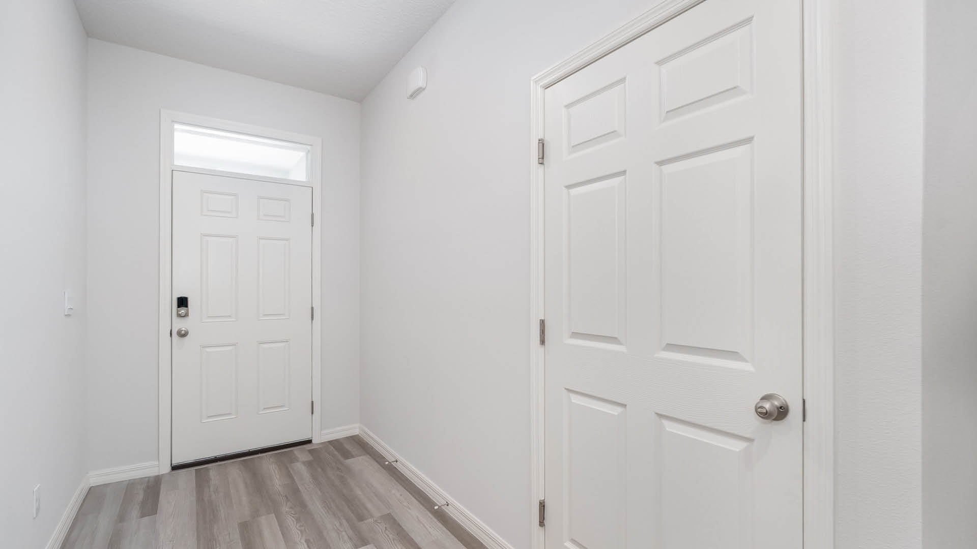 Bright and minimalistic hallway featuring a white front door, adjacent double closet doors, and light gray flooring.