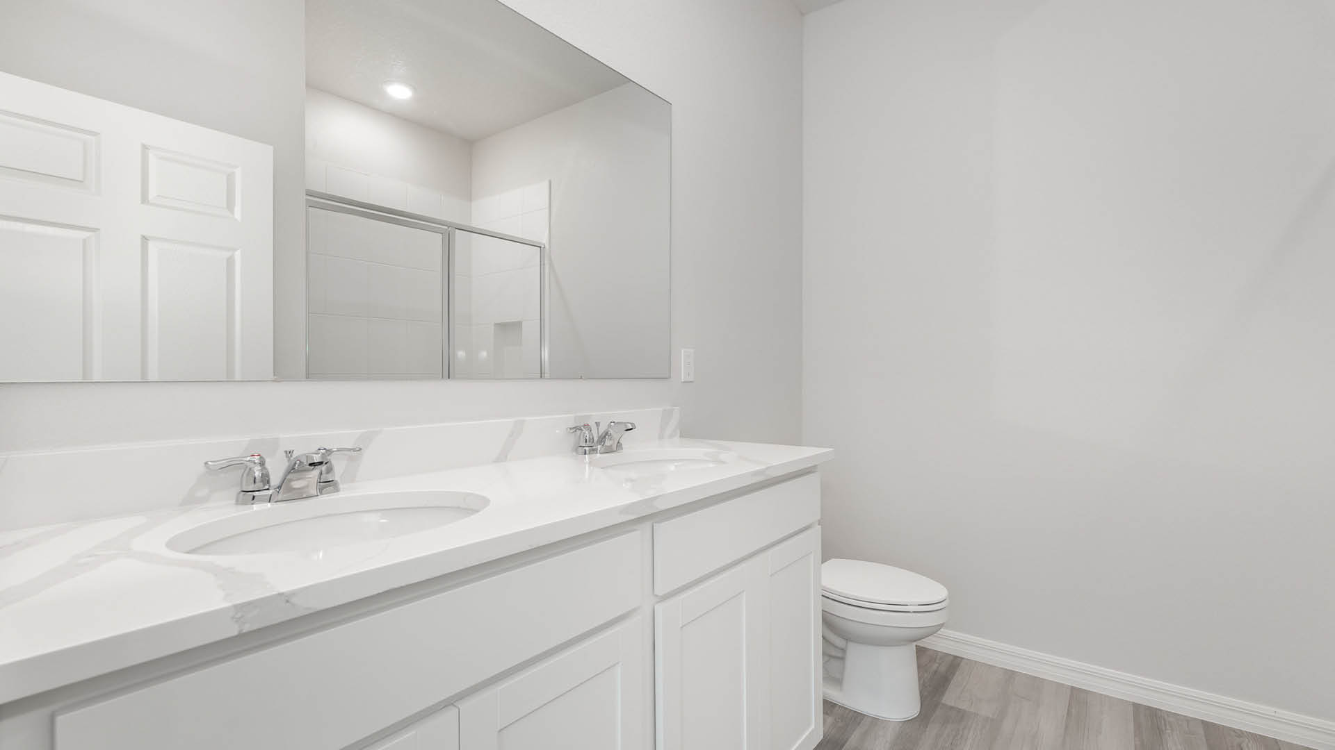 Modern bathroom featuring a double vanity with quartz countertop, a large mirror, white cabinetry, and a toilet in a neutral color scheme.