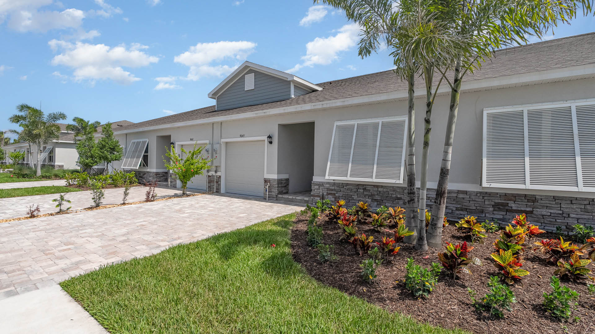 Exterior view of a modern single-story home with stone accents, tropical landscaping, and a blue sky in the background.