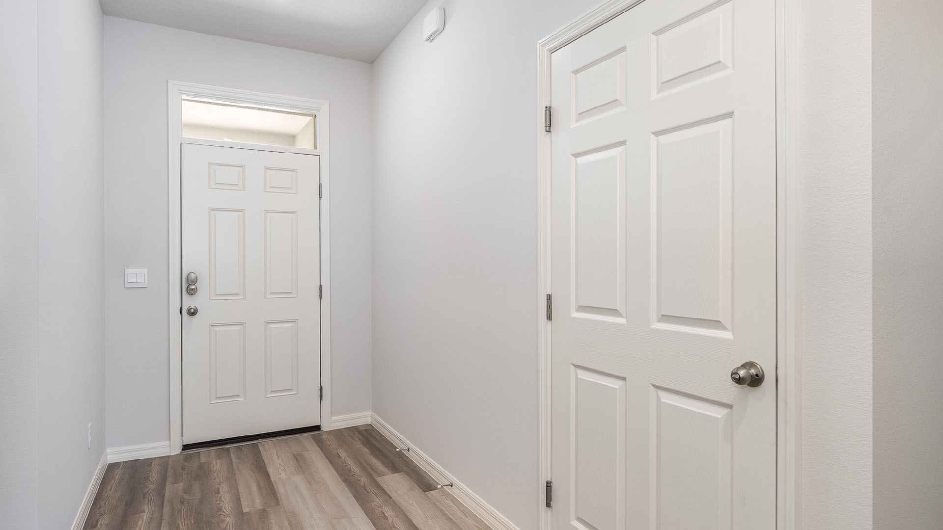 Bright and minimalistic hallway featuring a white front door, adjacent double closet doors, and light gray flooring.