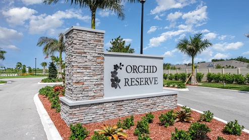 Entry sign for Orchid Reserve, featuring a stone and concrete structure surrounded by colorful landscaping under a blue sky.