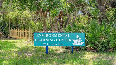 Sign for the Environmental Learning Center at 255 Live Oak Drive, surrounded by greenery and a wooden fence.