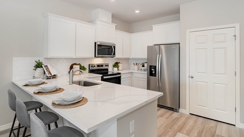 Modern kitchen featuring white cabinets, stainless steel appliances, quartz countertop, and stylish dining setup.