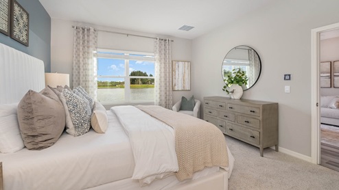 Bright and modern bedroom featuring a large window with a lake view, plush bedding, decorative pillows, and stylish furnishings.