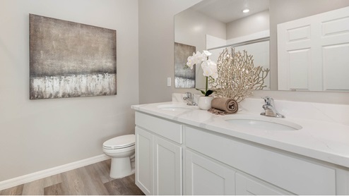 Modern bathroom with double sink vanity, white cabinetry, and large mirror. Decorative plant and painting add elegance. Neutral tones and vinyl plank flooring create a clean, calming atmosphere.