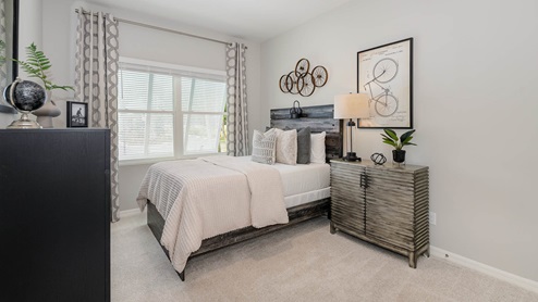 Cozy bedroom featuring a bed with plush pillows, a stylish nightstand, framed bicycle art, and large windows with sheer curtains.