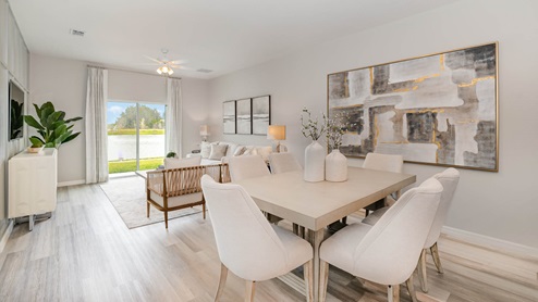Modern dining area with a light wood table, plush white chairs, a large artwork, and a view of a serene outdoor landscape.