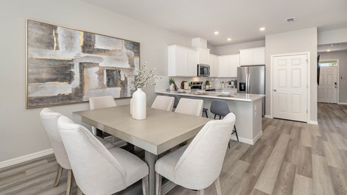 Kitchen overlooking dining room table. White cabinets, quartz countertops, vinyl plank flooring in neutral colors