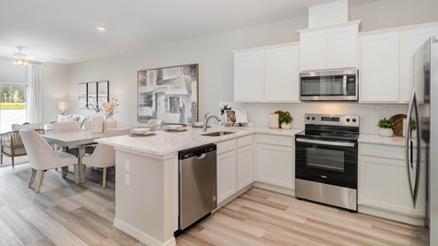 Modern kitchen with white cabinets, stainless steel appliances, and a dining area featuring light wood furniture and natural light.