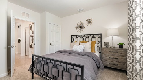 Cozy bedroom featuring a modern black metal bed, layered pillows, a nightstand with a lamp, and stylish wall decor.