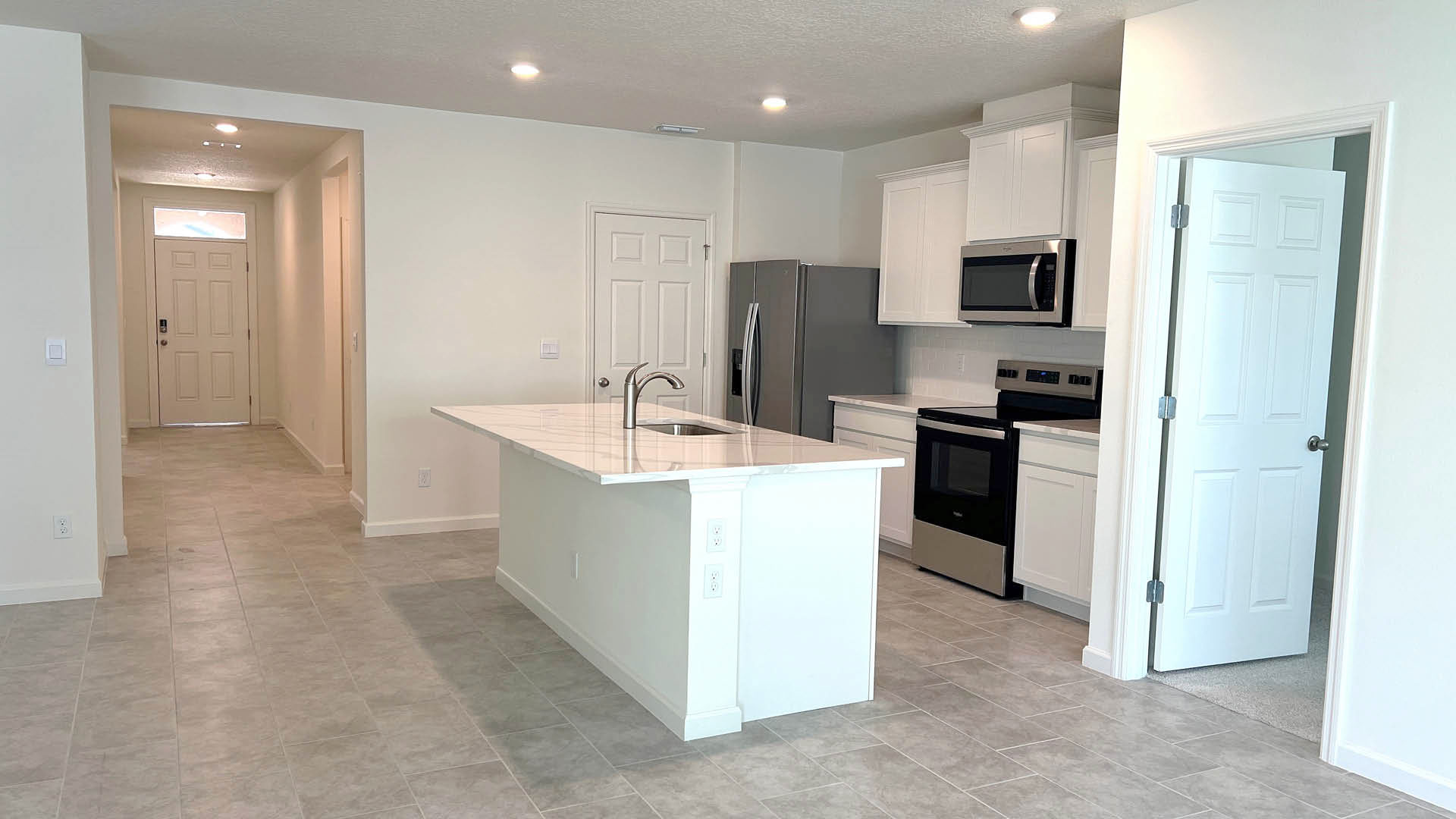 Modern kitchen with white cabinetry, stainless steel appliances, and an island, adjoined by a light-filled entryway.