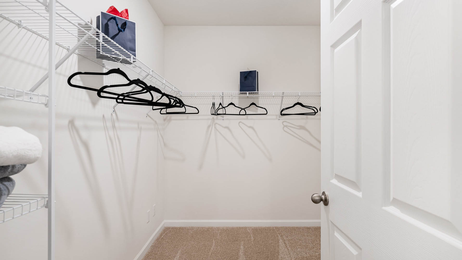 A spacious, empty closet with white wire shelving, black hangers, and neatly stacked towels on the floor, viewed from an open door.