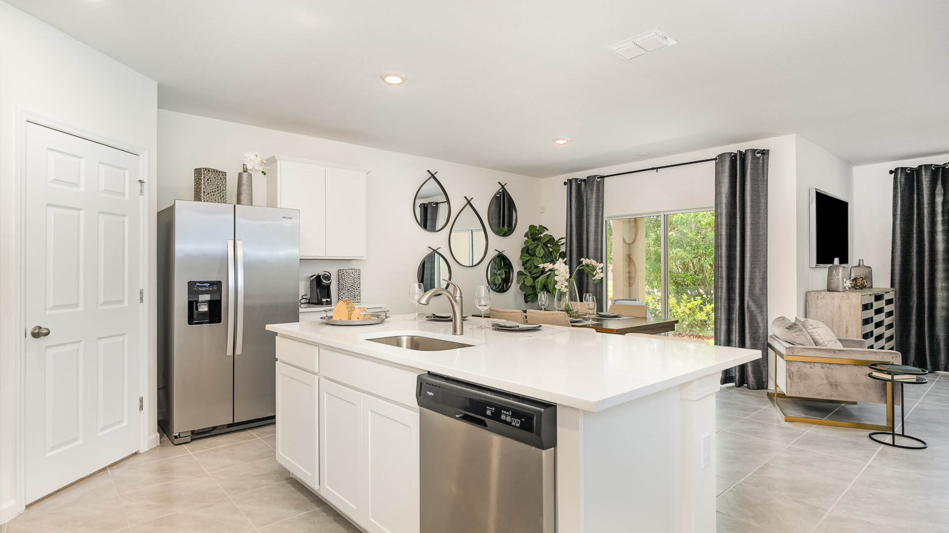 Modern kitchen featuring stainless steel appliances, white cabinetry, and stylish mirrors, with a cozy dining area and bright natural light.