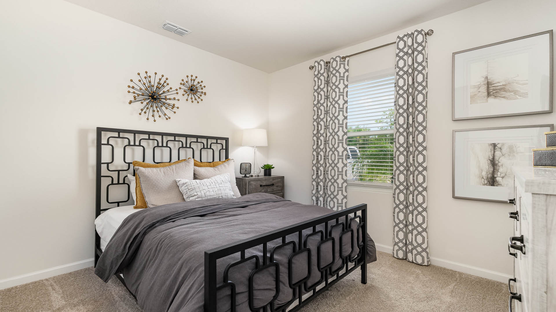 Cozy bedroom featuring a black metal bed frame, gray bedding, decorative pillows, and stylish curtains, with modern wall art and bright window.