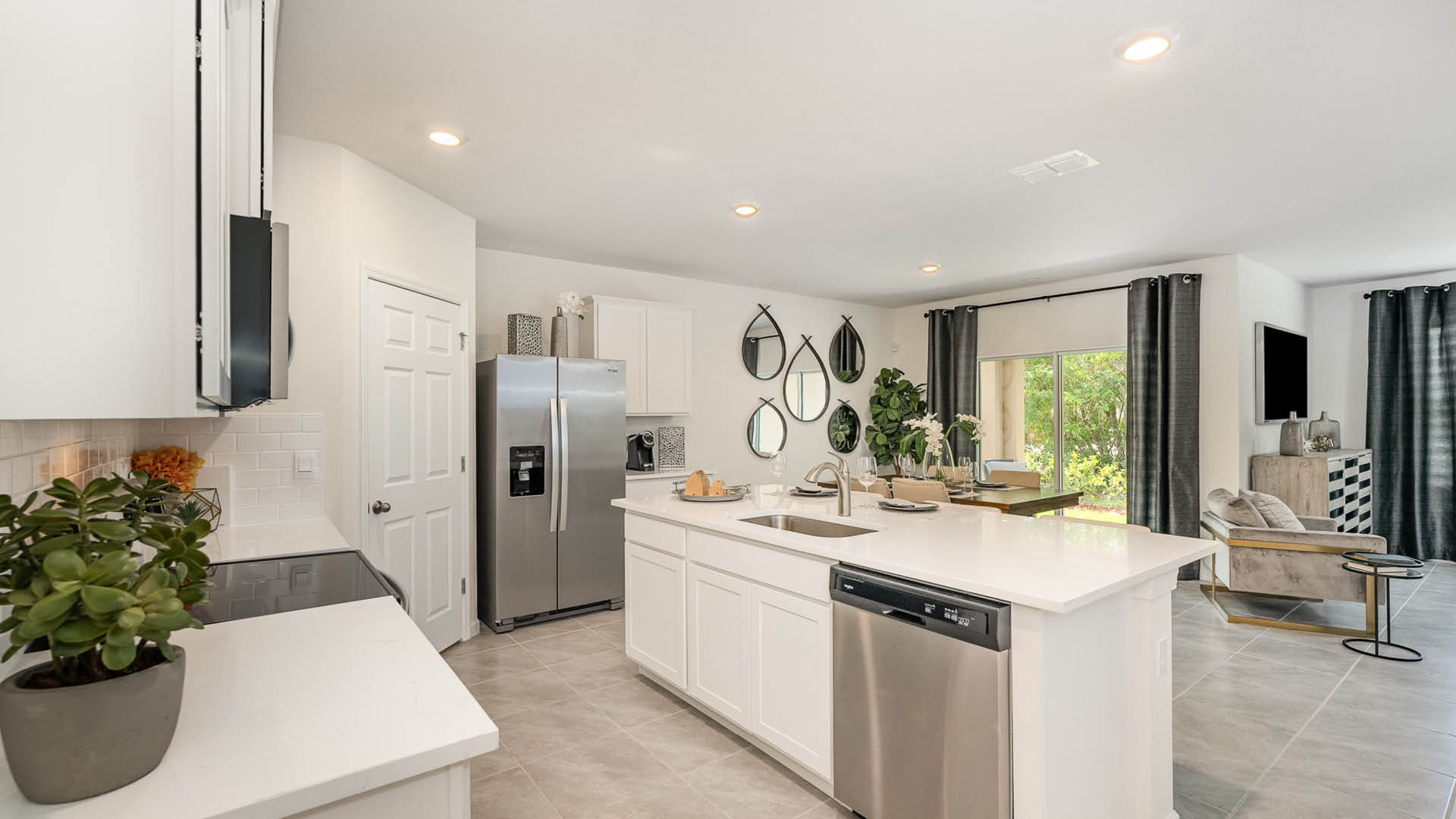 Modern kitchen with white cabinetry, stainless appliances, and natural light. Stylish decor includes plants and mirrors for a fresh look.