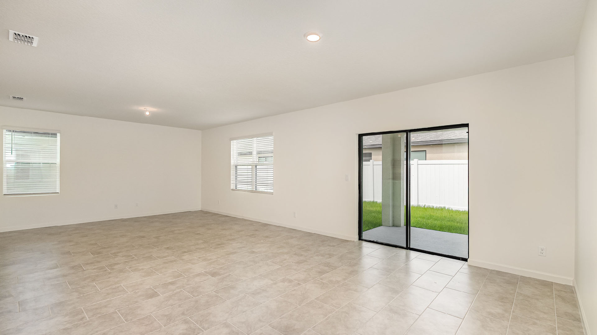 Spacious, bright living room with tiled floors, large windows, and sliding glass doors leading to a grassy outdoor area.