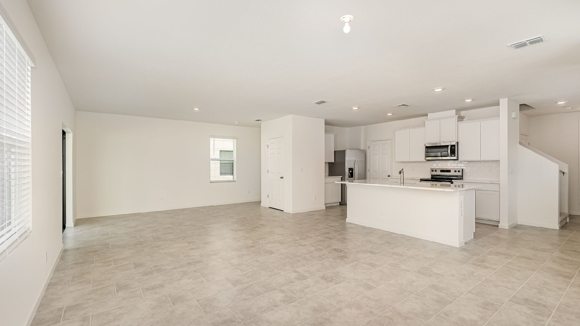 Spacious, open-concept living area with tiled flooring and modern kitchen featuring white cabinets and stainless steel appliances.