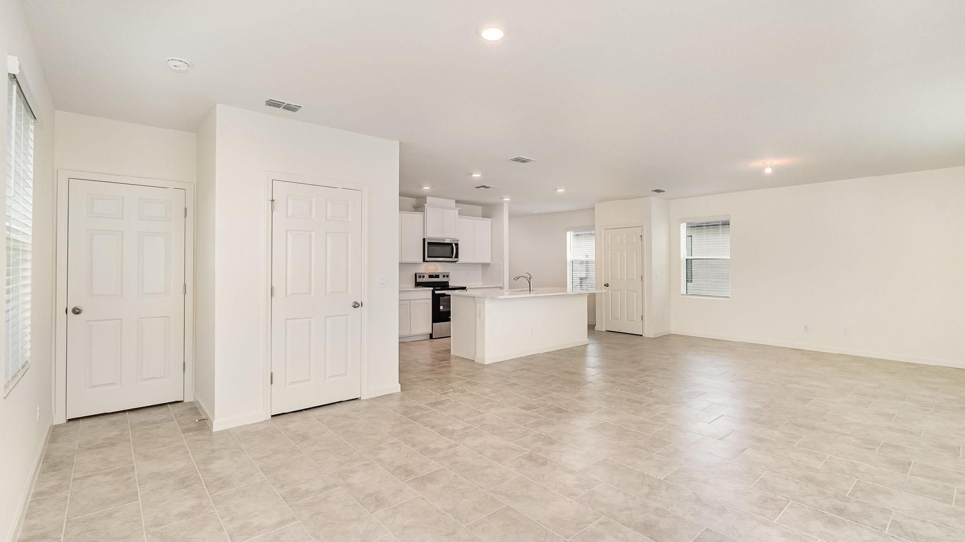 Spacious, modern open-concept living area with tiled flooring, kitchen island, and large windows for natural light.