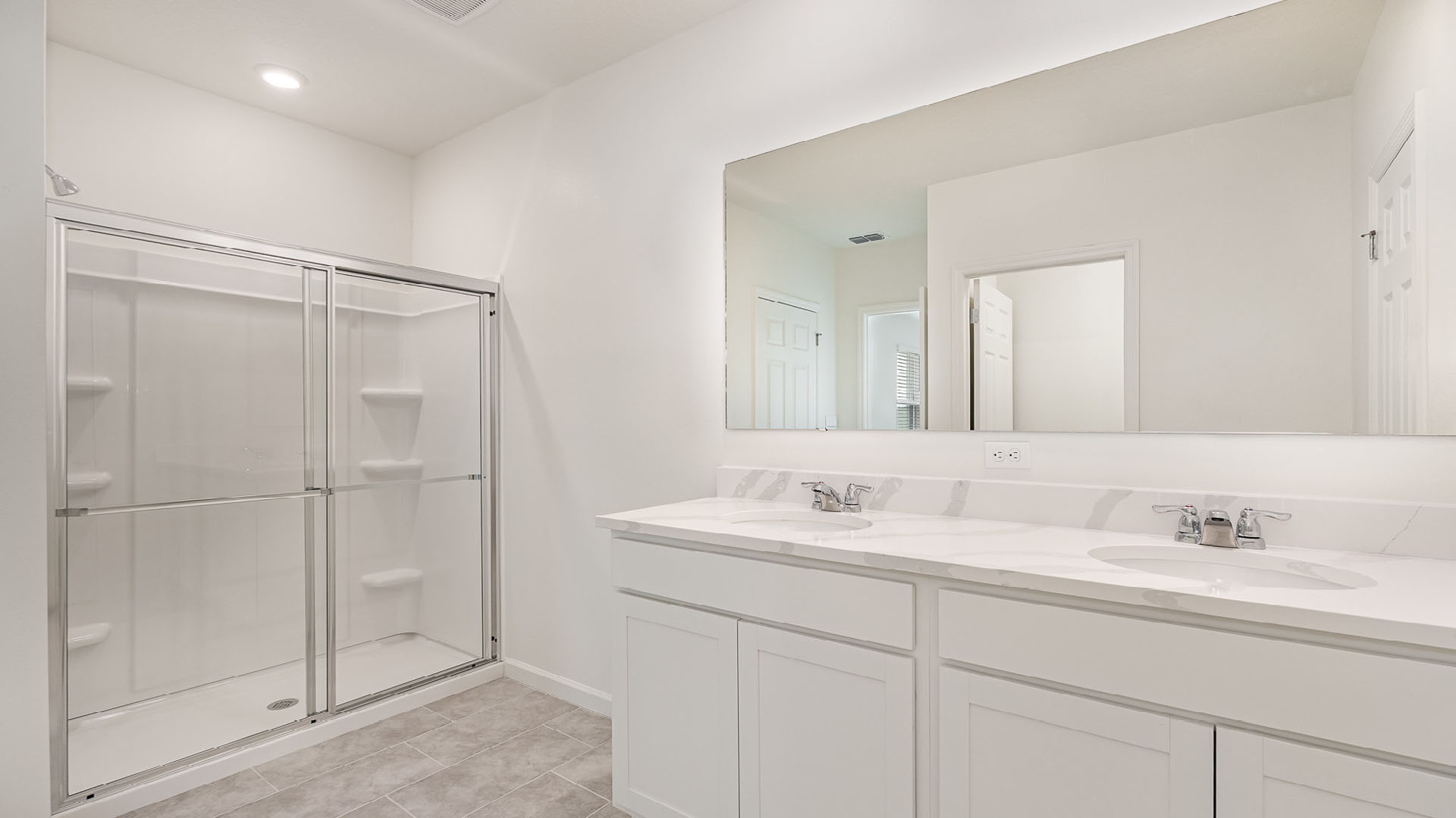 Bright, modern bathroom featuring a glass shower, dual sinks with marble countertop, and a large mirror against a white wall.