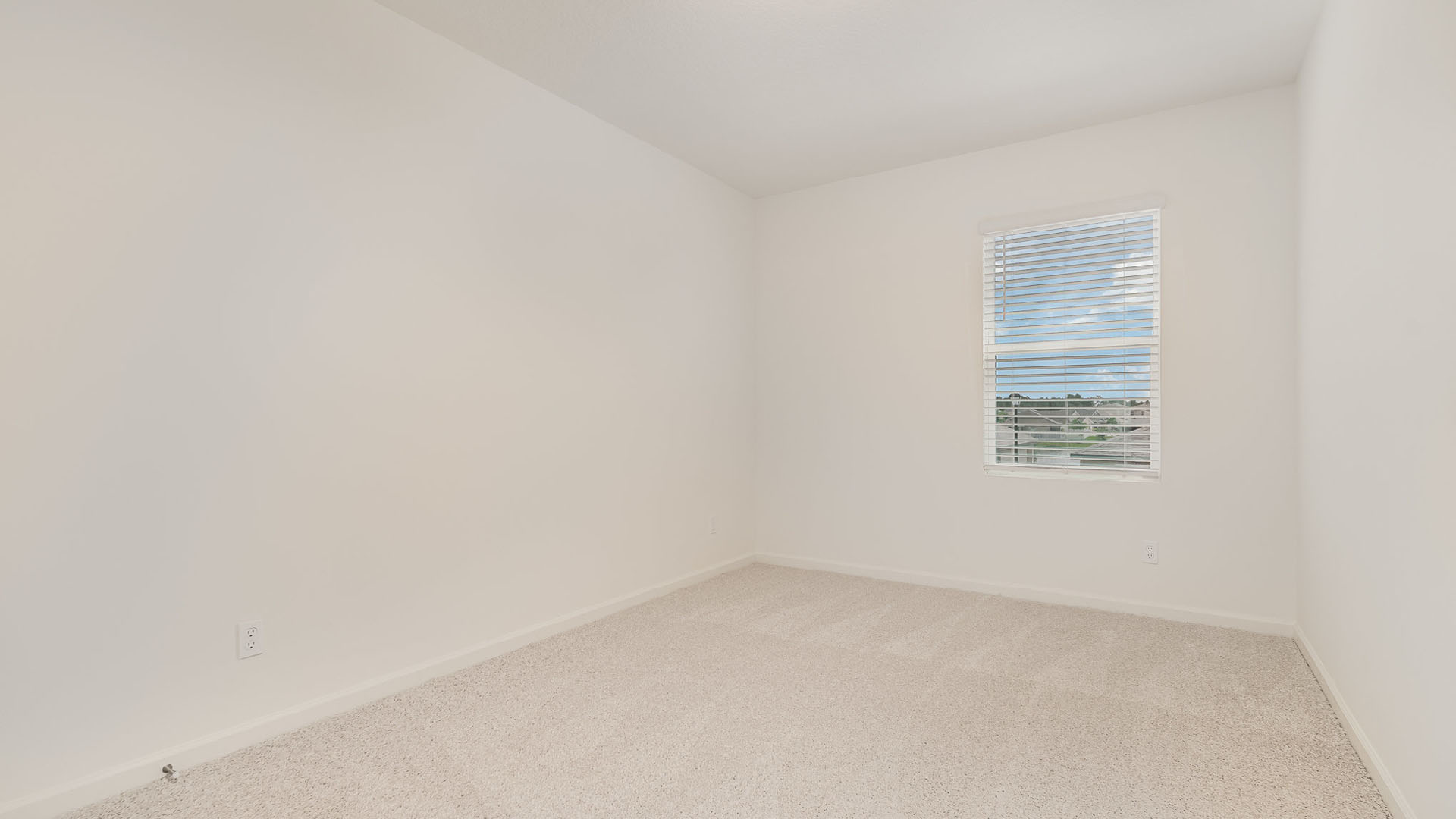 Empty room with light beige carpet, white walls, and a window with blinds letting in natural light. Clean and minimalistic space.
