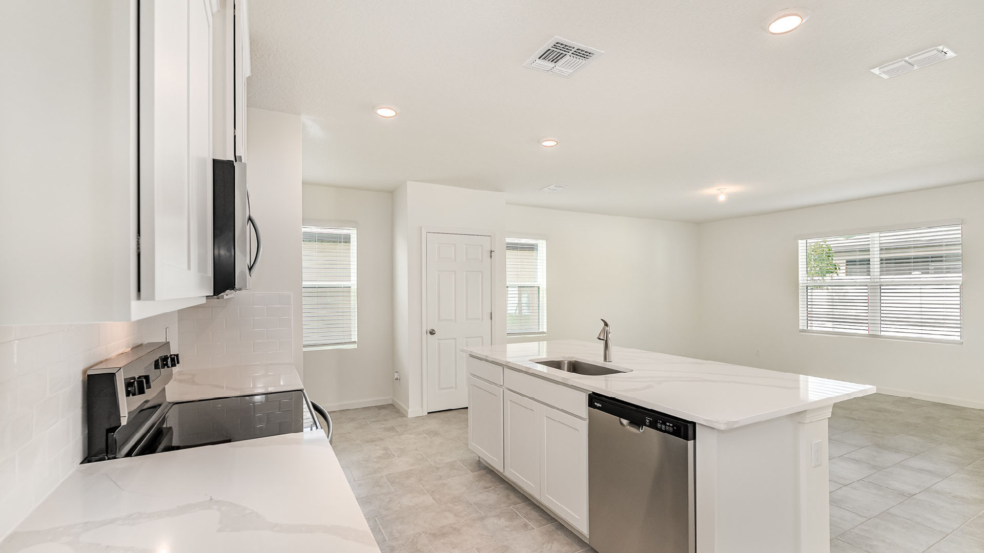Modern kitchen with white cabinetry, quartz countertop, stainless steel appliances, and an open layout to a bright, airy living space.