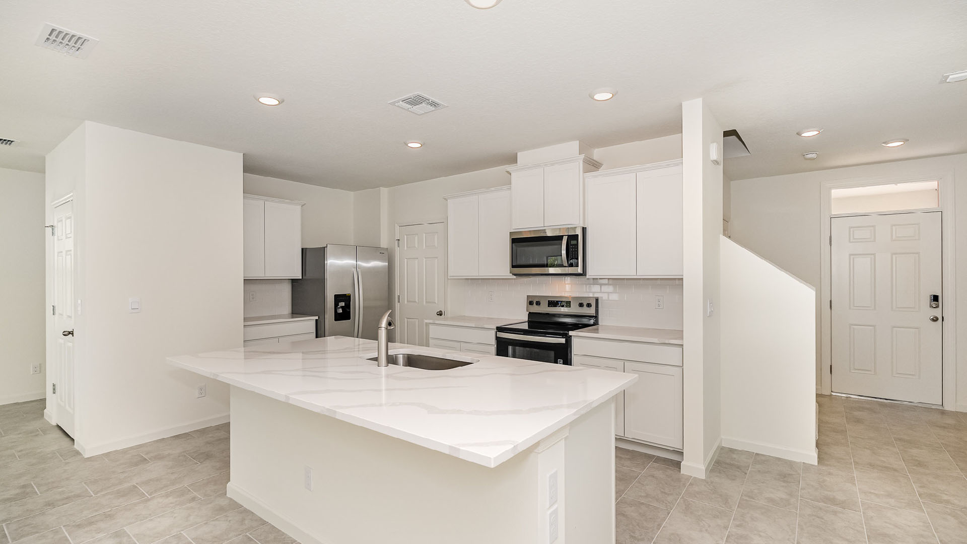 Modern kitchen with white cabinetry, stainless steel appliances, and a large marble island, featuring tile flooring and bright lighting.