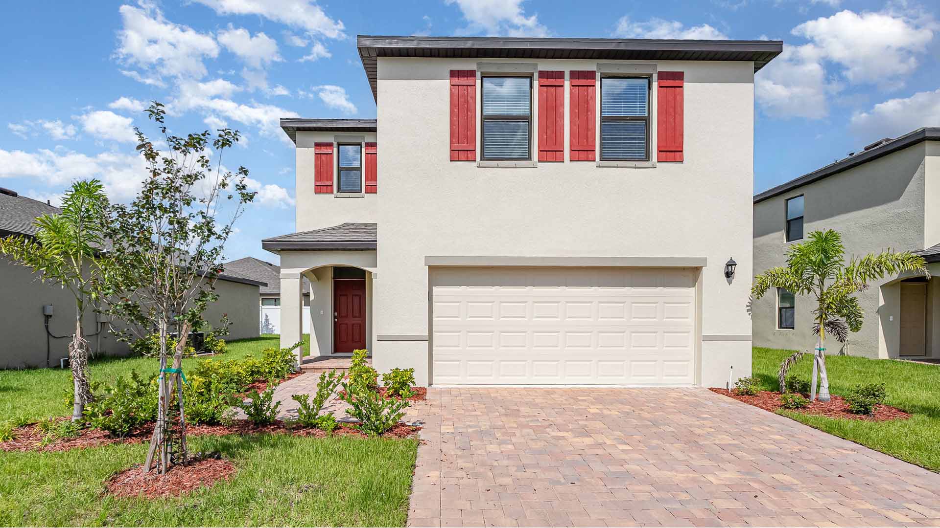 Modern two-story home with red shutters, a white garage door, and landscaped front yard featuring plants and a paved walkway.
