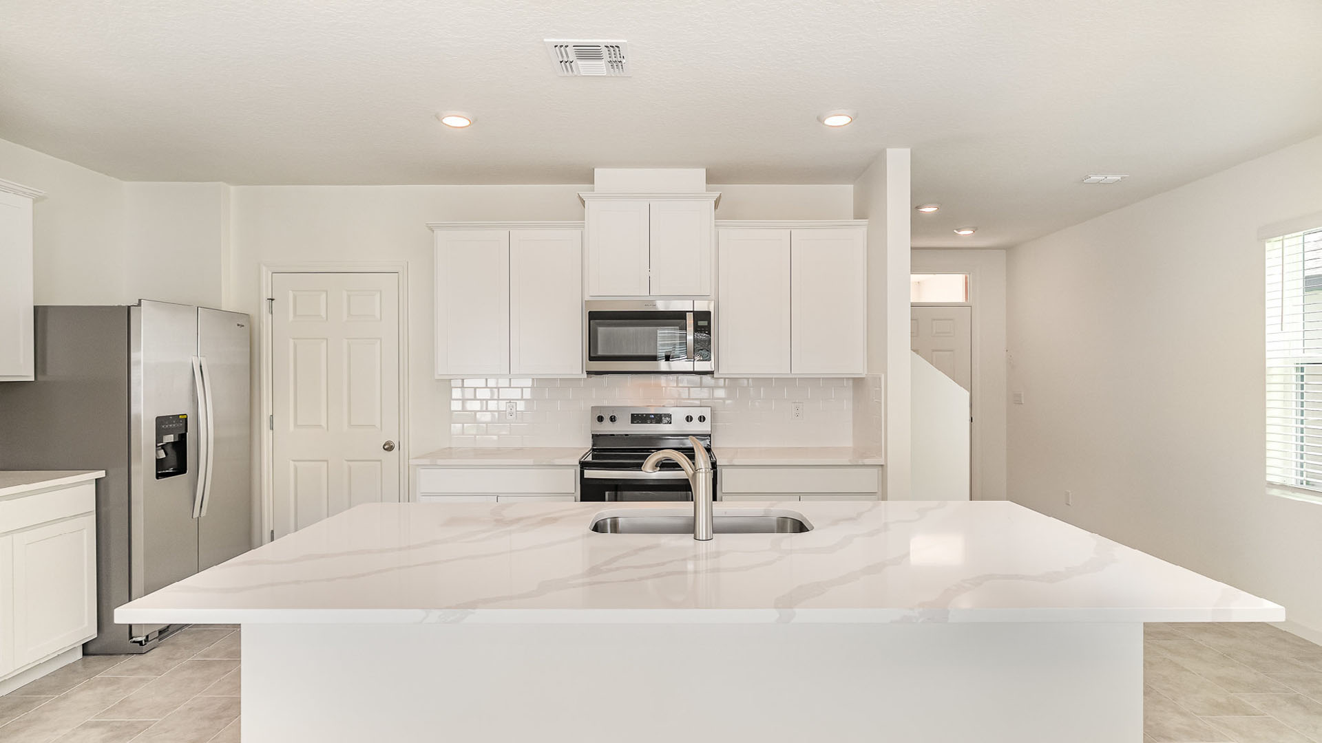 Bright, modern kitchen featuring white cabinetry, stainless steel appliances, and a spacious island with a quartz countertop.
