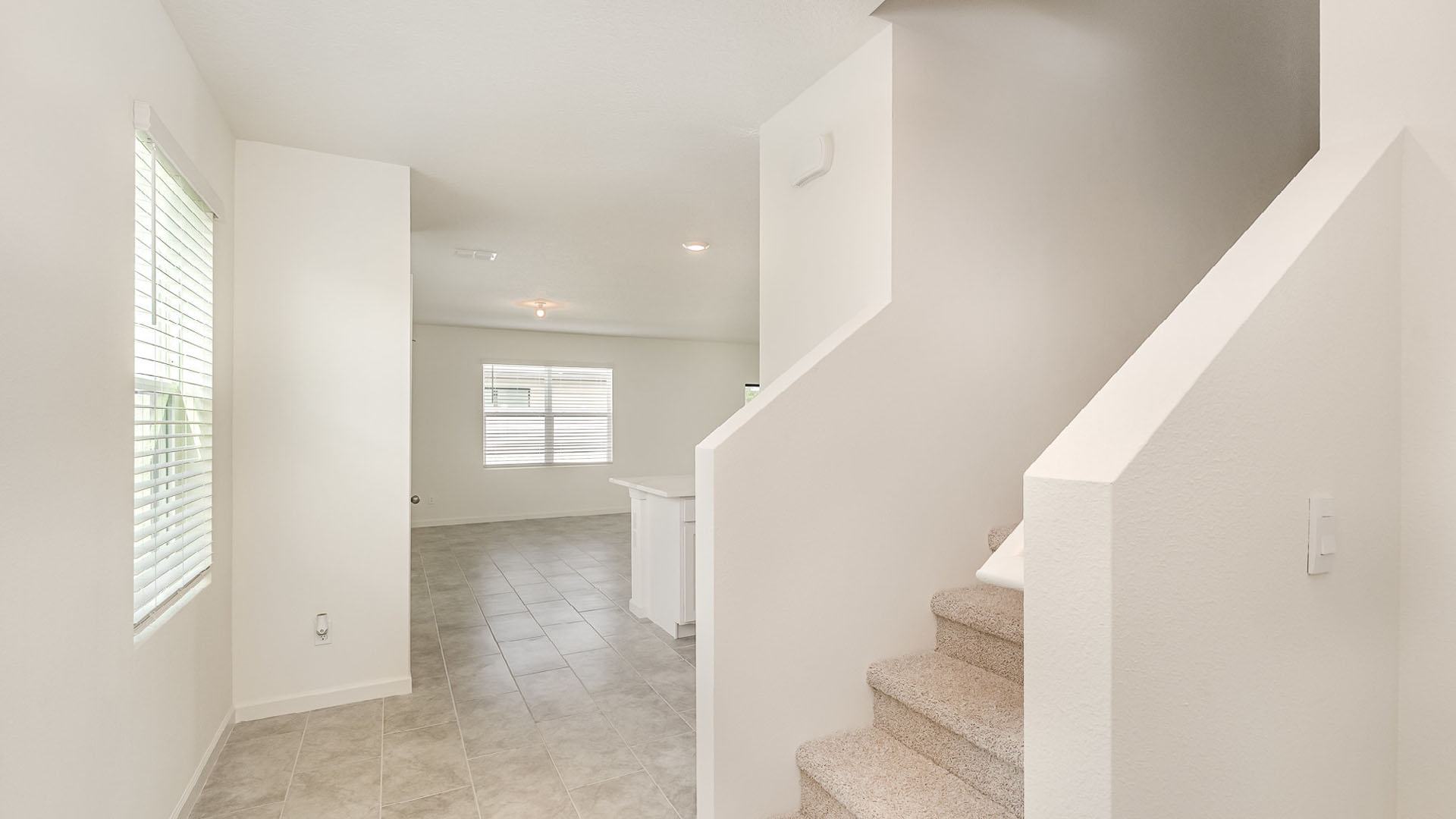 Bright, spacious interior entrance featuring stairs, tile flooring, and large windows with blinds in a modern design home.