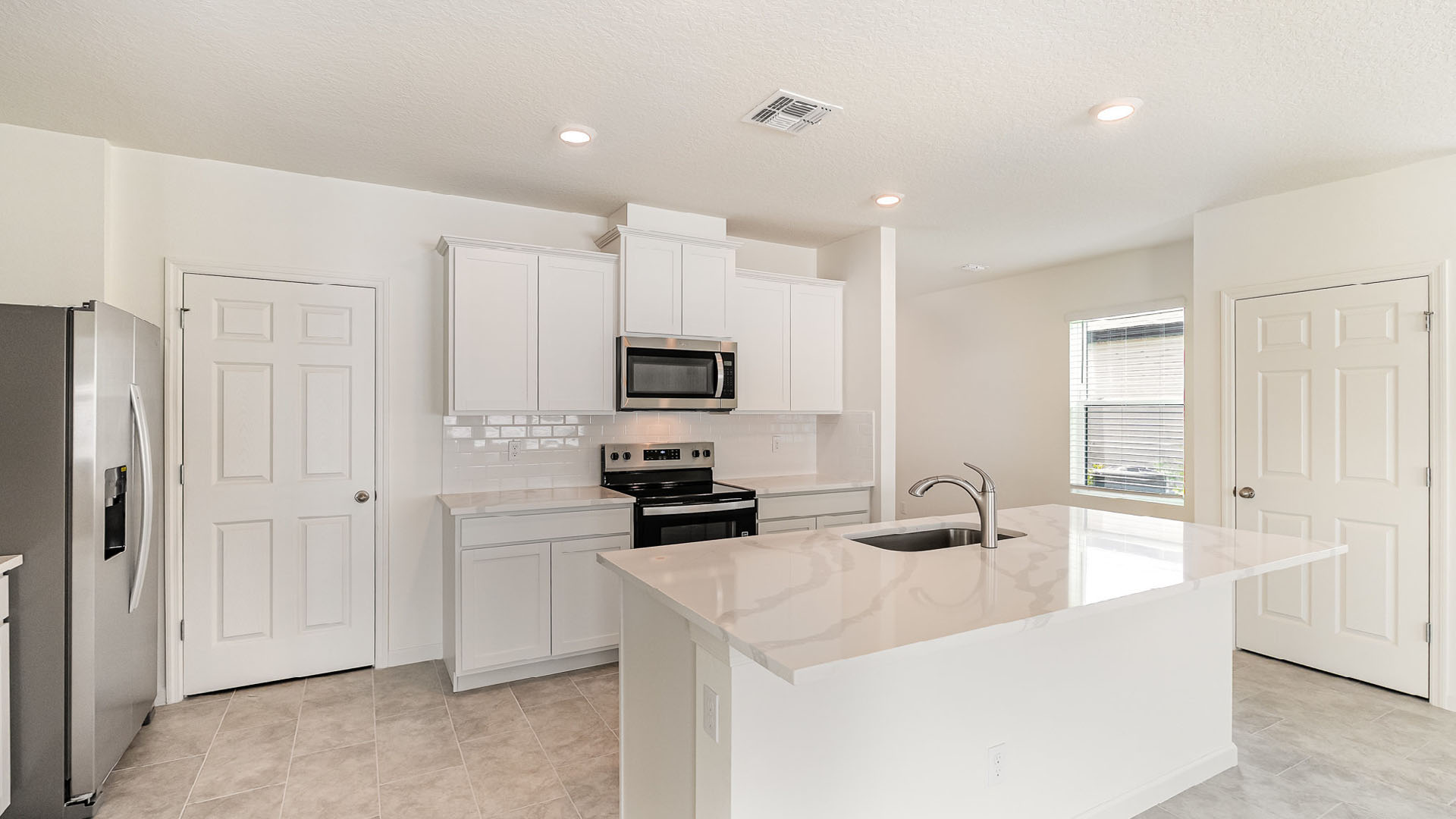 Modern kitchen featuring white cabinets, stainless steel appliances, a large island with a sink, and tile flooring in a bright space.