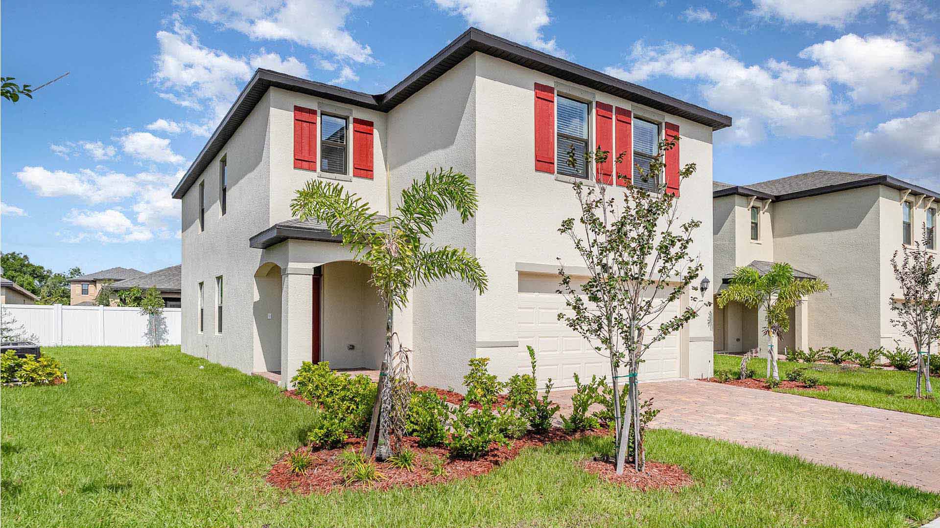 Two-story beige house with red shutters, well-maintained front yard, and drivewa.