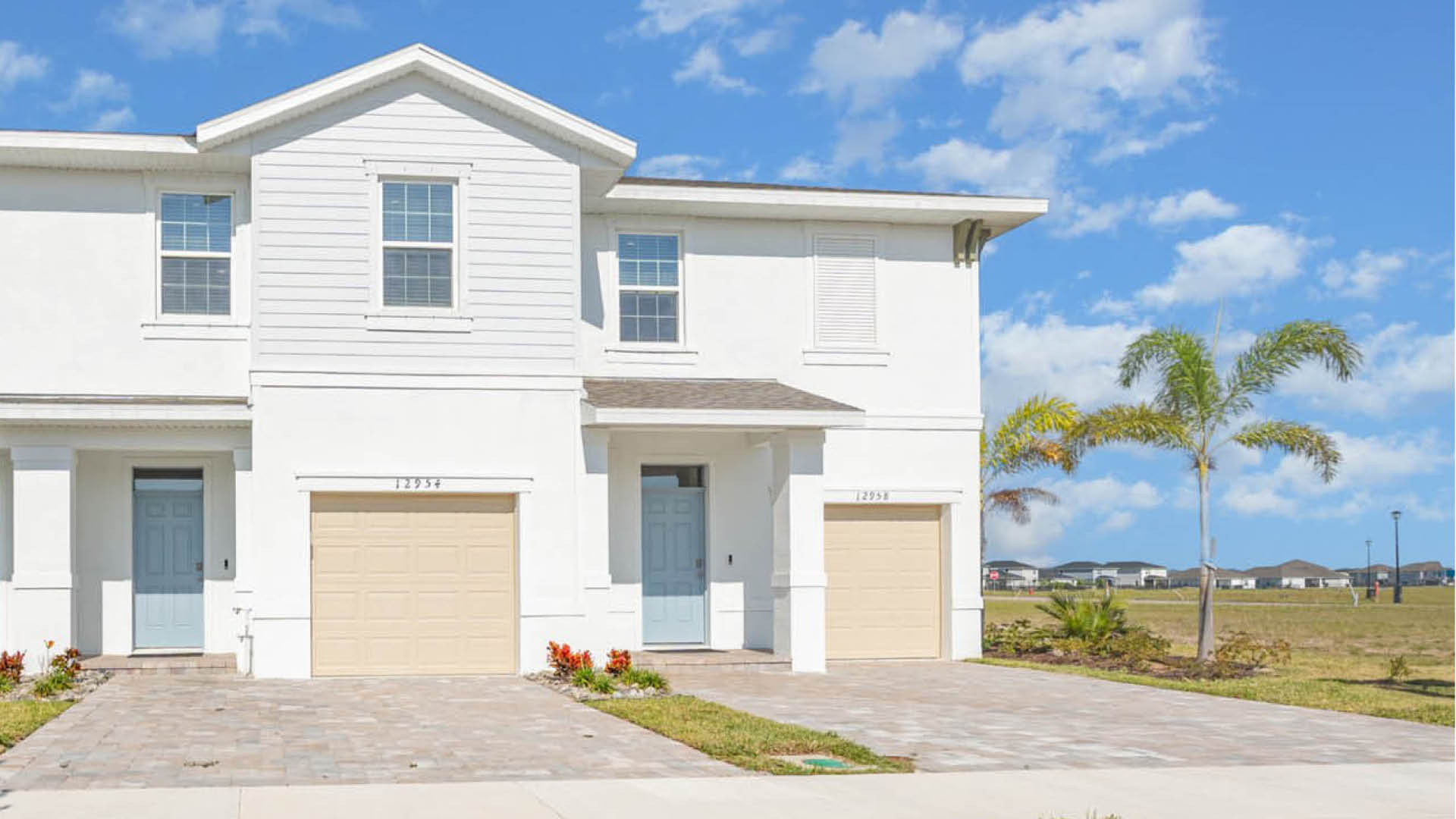 Central Park Townhomes Exterior with light blue front door, beige one-car garage and paver driveway.