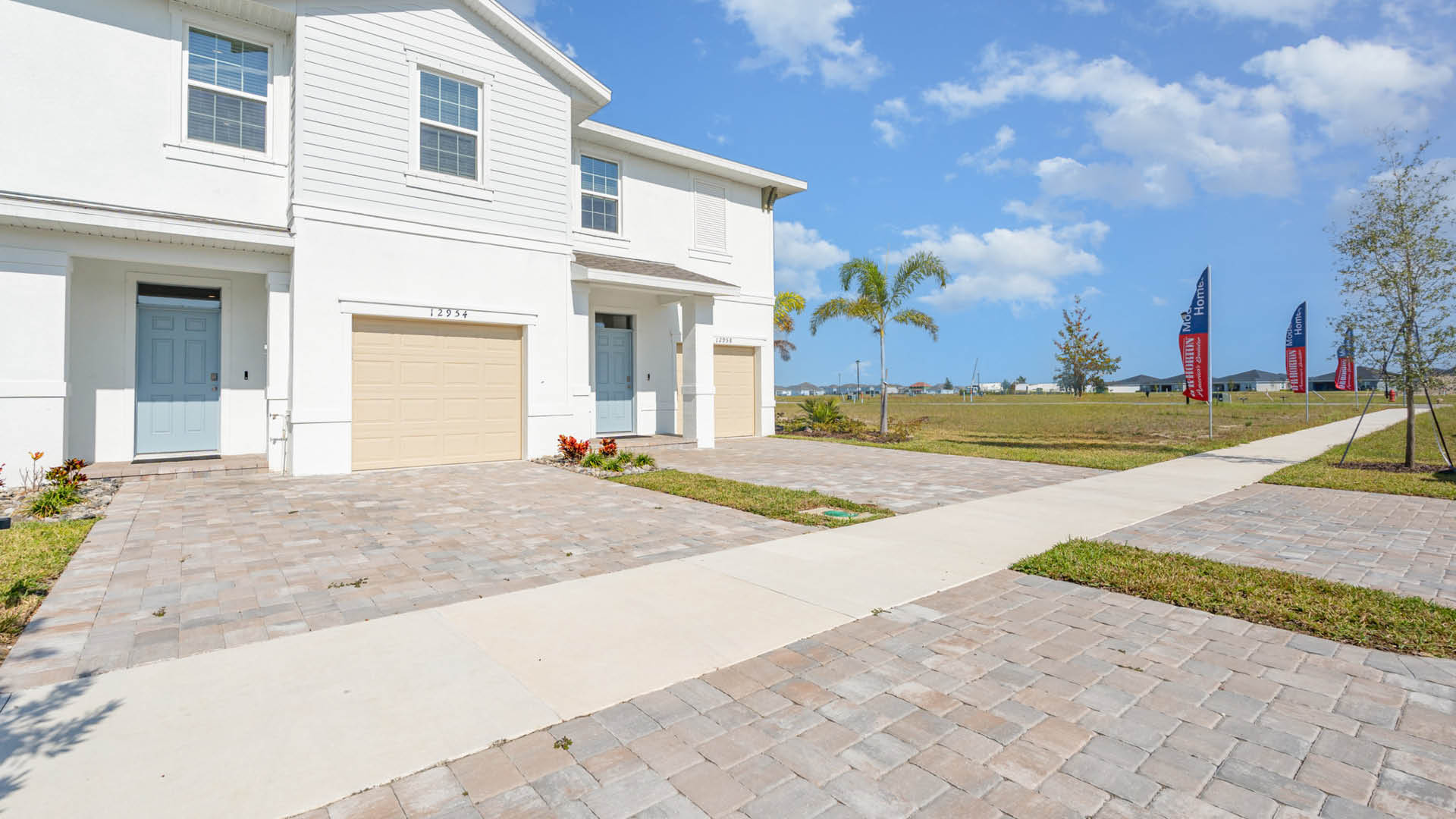 Street view of Central Park Townhomes Exterior with light blue front door, beige one-car garage and paver driveway.