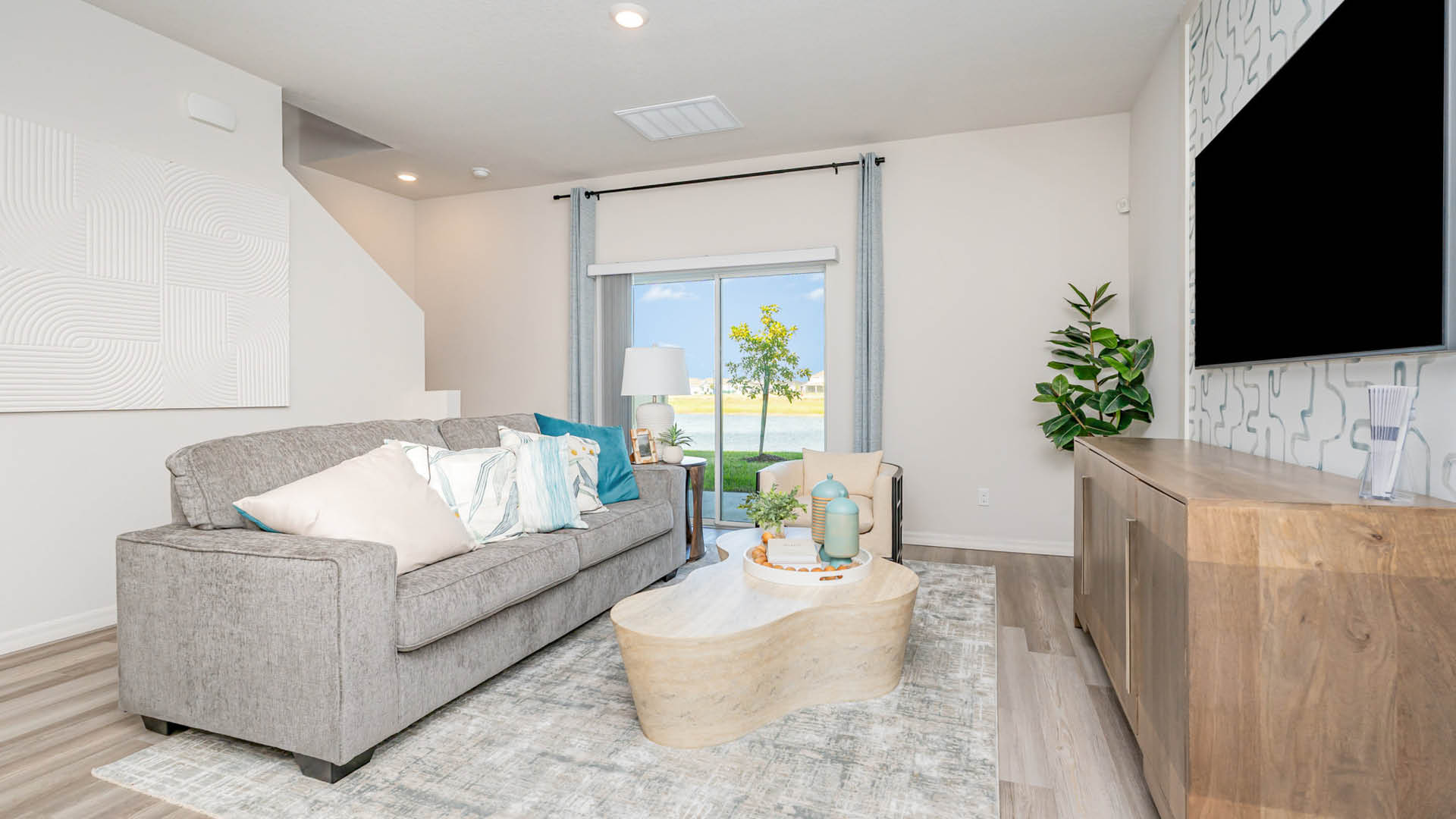 Modern living room with a gray sofa, decorative pillows, a unique coffee table, and large window showcasing a scenic view.