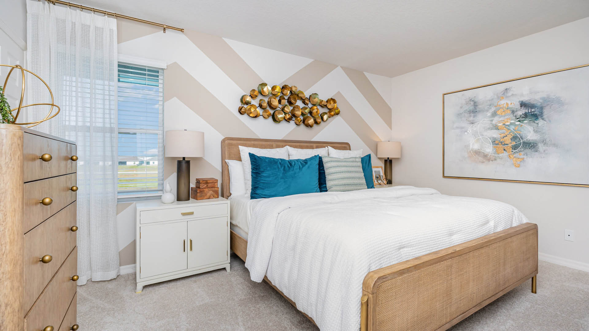 Cozy bedroom featuring a layered white bedspread, teal pillows, wooden furniture, and modern decor against a chevron wall.