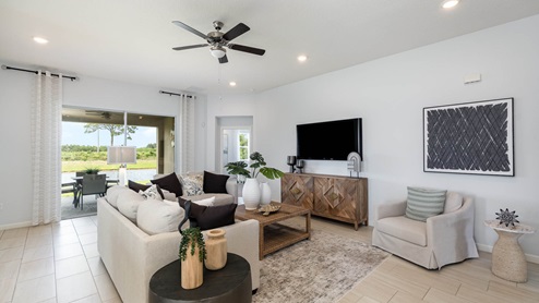 Bright and airy living room featuring a light sofa, wooden decor, a TV unit, and views of greenery through large sliding glass doors.